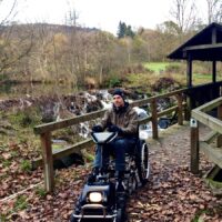 Dr. Holger Tülp testet ein Gespann aus Rollstuhl und Zuggerät auf dem zertifizierten barrierefreien Komfort-Weg rund um den Stausee Irrhausen. Bildquelle: Naturpark Südeifel/Dr. Holger Tülp.