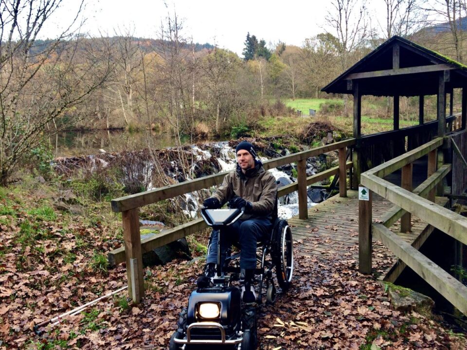 Dr. Holger Tülp testet ein Gespann aus Rollstuhl und Zuggerät auf dem zertifizierten barrierefreien Komfort-Weg rund um den Stausee Irrhausen. Bildquelle: Naturpark Südeifel/Dr. Holger Tülp.