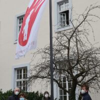 Auch in der Corona-Krise hängt die Red-Hand-Flagge vor dem Rathaus. OB Wolfram Leibe (l.) hisste sie zusammen mit Schülern vom FWG, HGT und der IGS. Bildquelle: Presseamt Trier