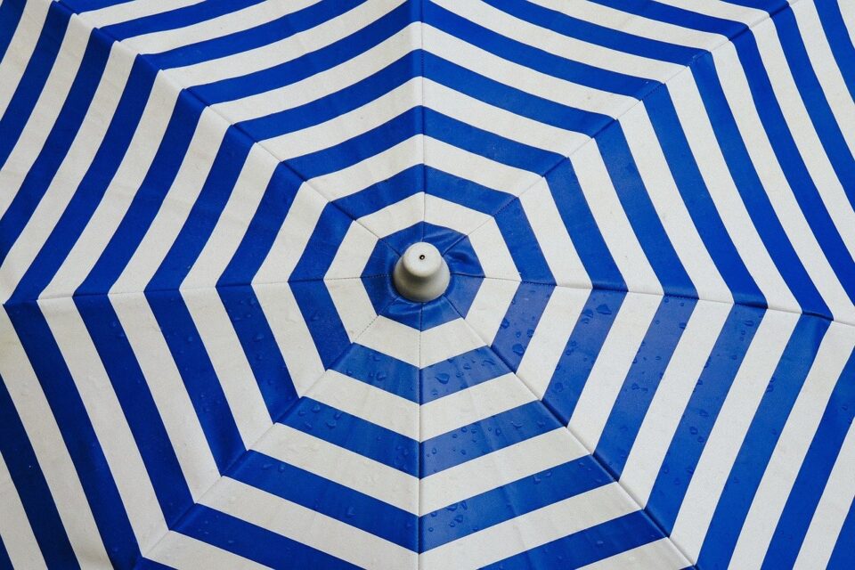 Das Bild zeigt einen blau weiß gestreiften Sonnenschirm von oben. Foto: Free-Photos auf Pixabay