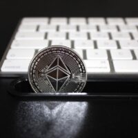 Das Foto zeigt eine Bitcoin Münze vor einer Tastatur auf einem schwarzem Tisch. Foto: Pexels.com