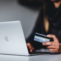 Auf dem Foto nutzt eine Frau ihre Kreditkarte an einem Macbook zur Onlinezahlung. Foto: Pickawood on unsplash