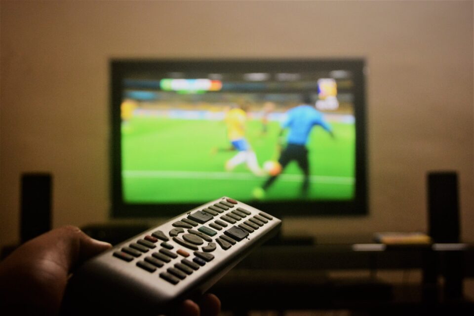 Jemand schaltet mit dr Fernbedienung das Fussballspiel im Fernseher um. Foto: pexels-soumith-soman