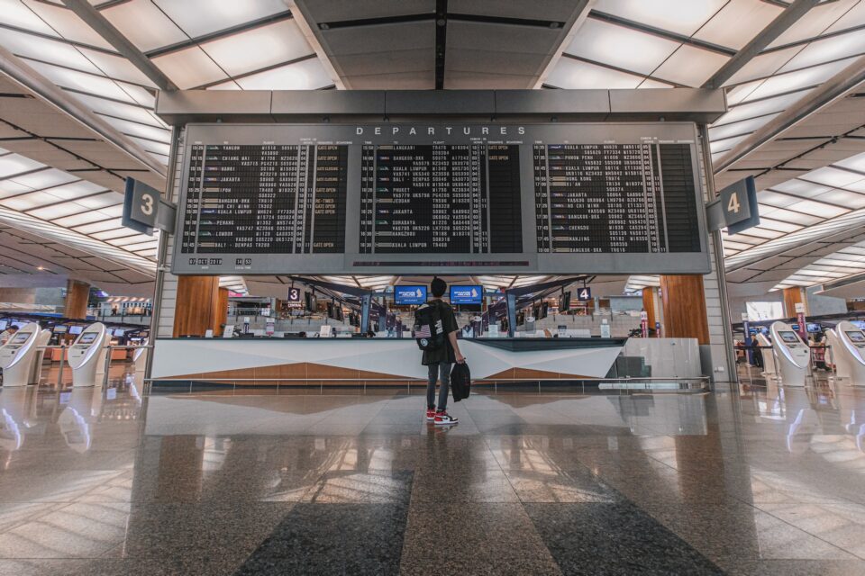 Flughafen - eine Person steht vor der Abflug und Ankunststafel. Foto: Daniel Lim on Unsplash