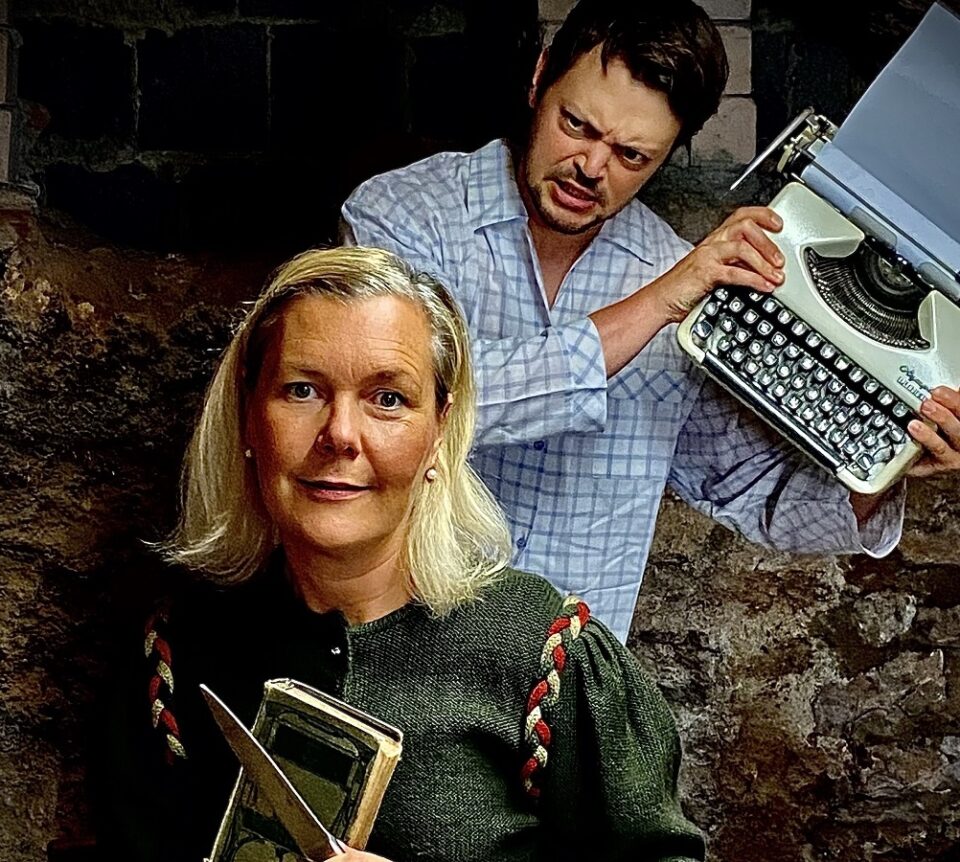 Ein Mann steht mit einer Schreibmaschine hinter einer Frau, die ein Messer und ein Buch in der Hand hält. Foto: Stephan Vanecek