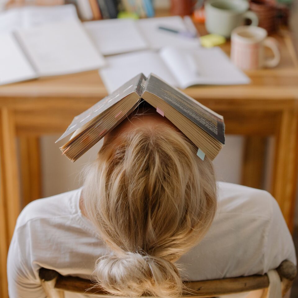 Eine Studentin steckt frustriert ihr Gesicht in ein Buch. Foto: cottonbro studio/Pexels