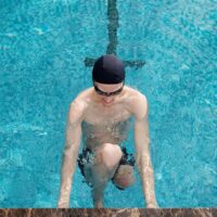 Person mit schwarzer Badekappe und Taucherbrille steigt ins Becken. Foto: ShotPot/ Pexels