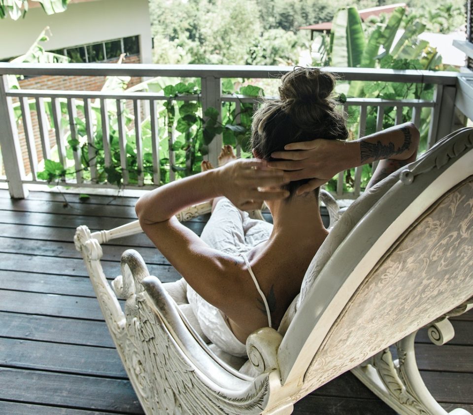 Eine Person sitzt in einem Schaukelstihl auf einem Balkon. Foto: Nastia Ligrain/ Pexels