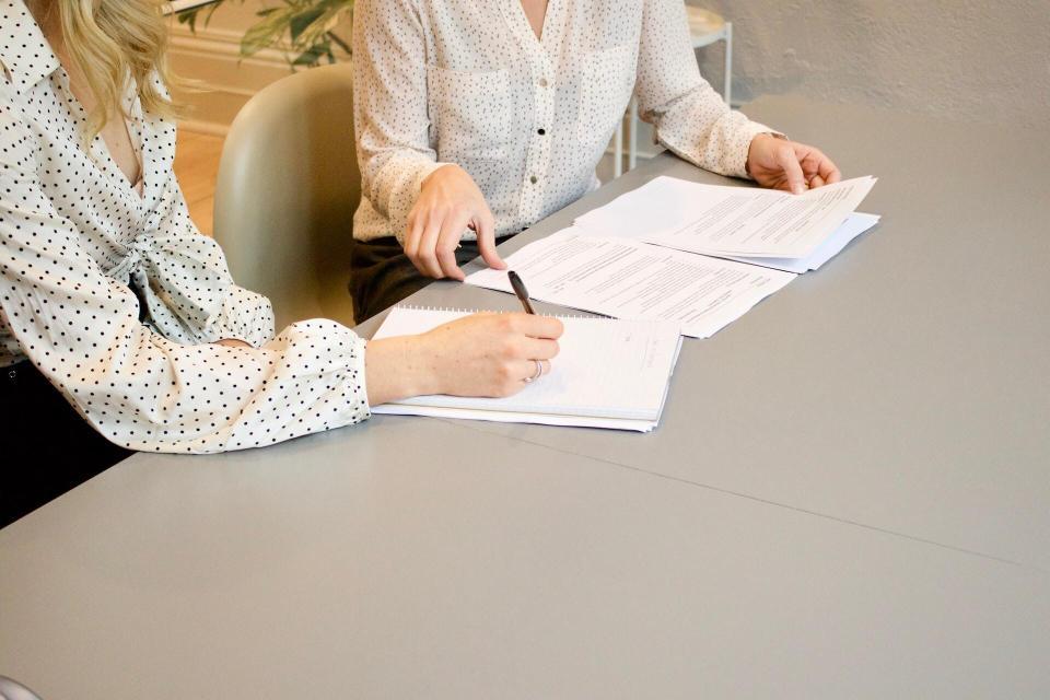 Frau unterschreibt auf weißem Druckerpapier neben Frau, die die Dokumente berühren will. Foto: gabrielle-henderson via unsplash
